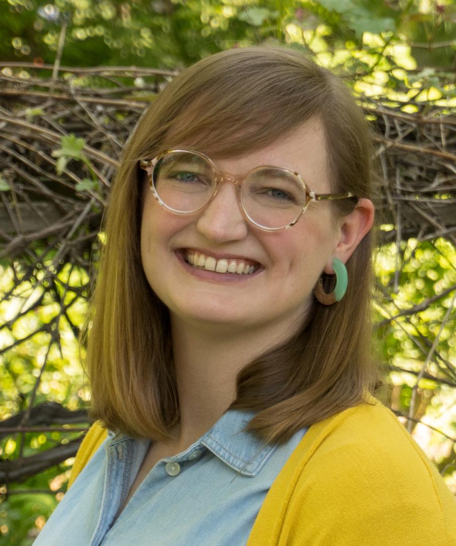 headshot of Kara Whittaker wearing a yellow sweater in front of trees